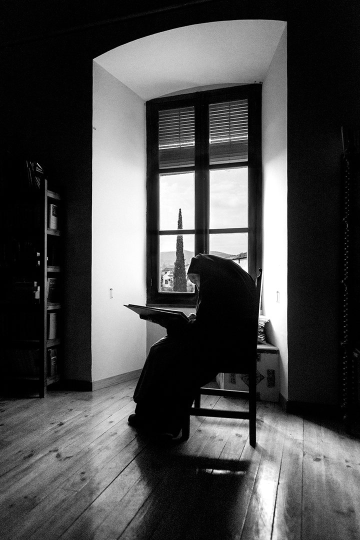 A nun sitting beside a window in a room.